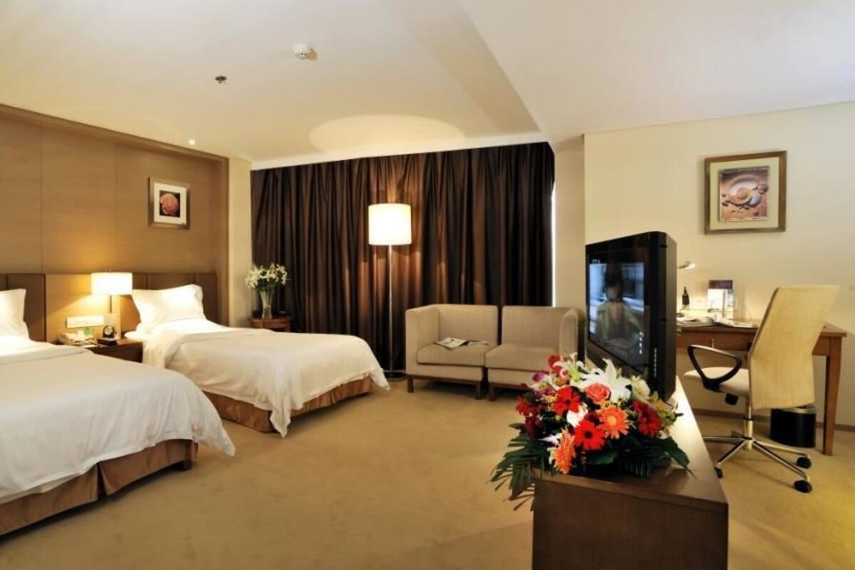 A hotel room with two beds, a sofa, a desk with a computer, and a TV.