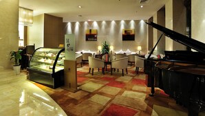 A hotel lobby with a grand piano, a dessert display, and a seating area with tables and chairs. - Roying Hotel (Wuhan)