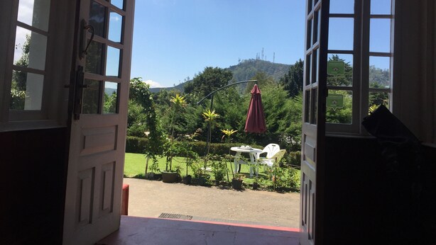 Un portal abierto que da a un jardín con una mesa y sillas, rodeado de follaje y una vista de una colina.