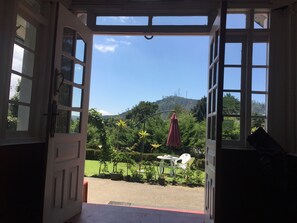 An open doorway leading to a garden with a table and chairs, surrounded by greenery and a view of a hill. - The Trevene Hotel (Nuwara Eliya)