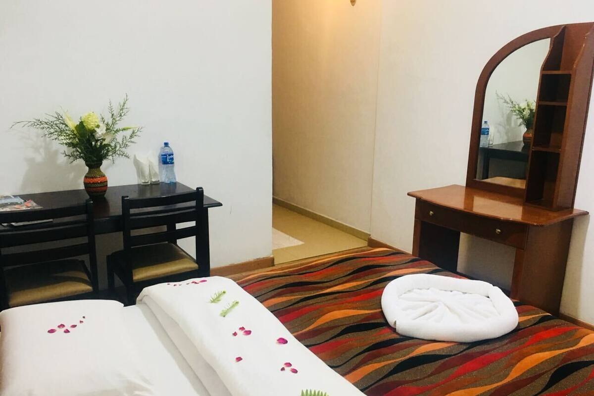 Une chambre d’hôtel avec deux lits, un bureau, une chaise, un miroir et une petite plante en pot.
