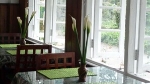 Comedor con mesa de vidrio, sillas de madera y un jarrón con flores blancas.