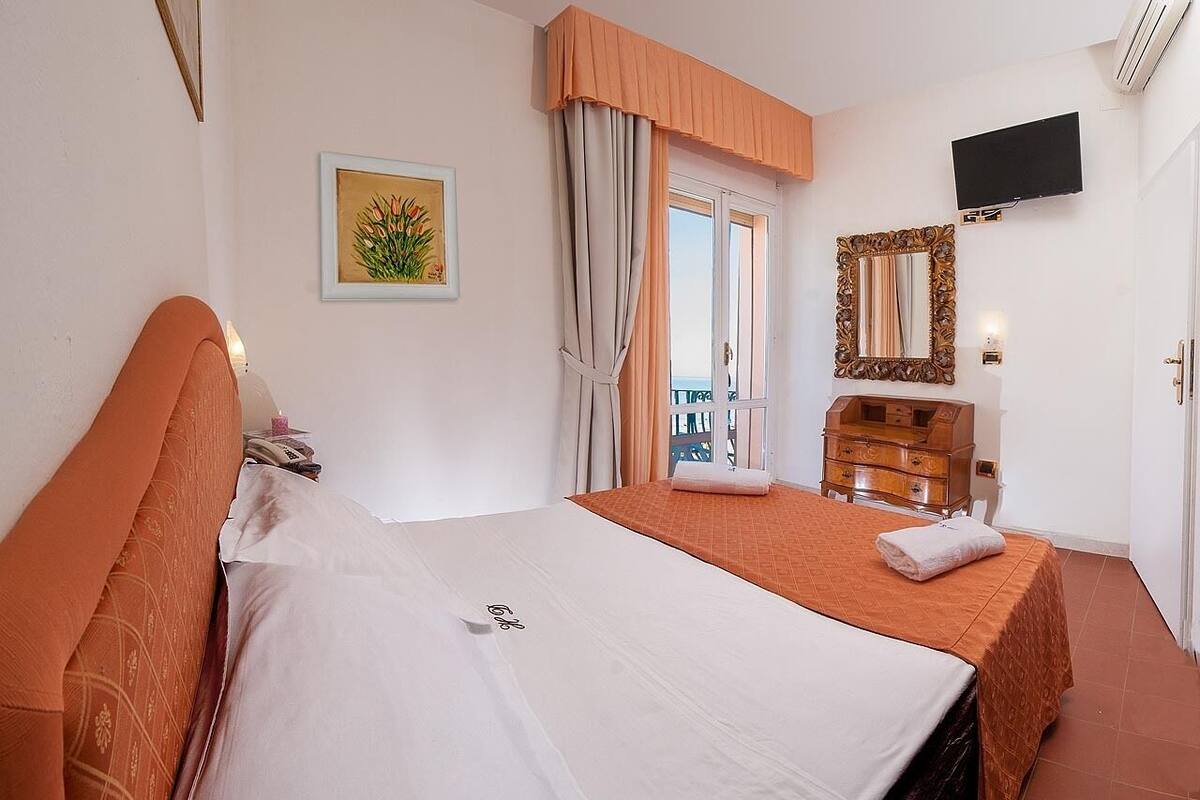 A hotel room with a bed, a dresser, a TV, and a window with curtains.