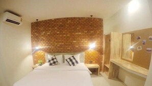 Una habitación de hotel con una pared de acento de ladrillo, una cama con ropa blanca, una mesita de noche y un espejo.