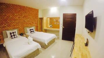 A hotel room with two beds, a wooden bench, a TV, and a brick wall.