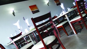 A restaurant interior with multiple tables and chairs, white tablecloths, and a painting on the wall. - Hotel LaBama (Gaborone)