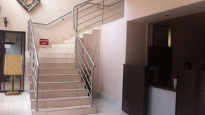 A staircase with metal railings, a sign that reads "MIND YOUR STEP," and a reception desk area. - Hotel LaBama (Gaborone)