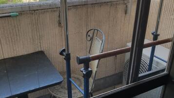 A balcony with a table and chair, a metal railing, and a view of the street and buildings.