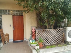 A building entrance with a wooden door, a signboard, a potted plant, and a lattice fence. - Guesthouse Kazenoie Bonita - Caters to Women (Sennan)