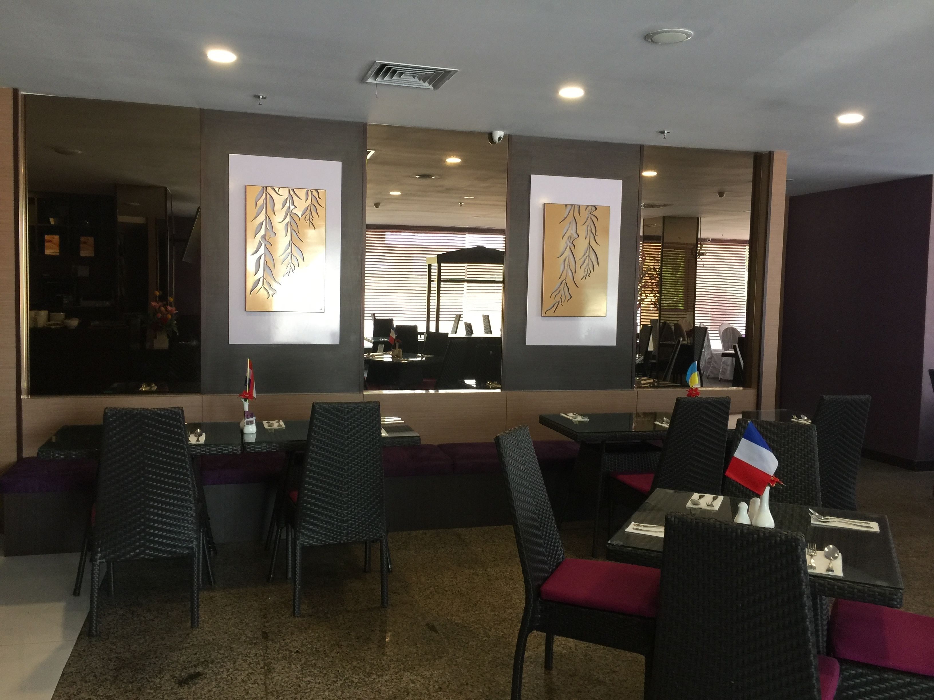 A restaurant with dark wicker chairs and red cushions, a glass partition, and artwork on the walls.