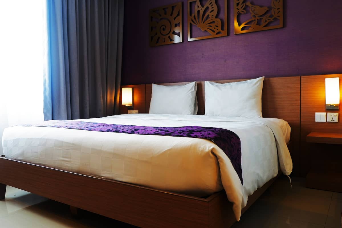 Een hotelkamer met een groot bed, een houten hoofdeinde, een paarse accentmuur en decoratieve wandkunst.