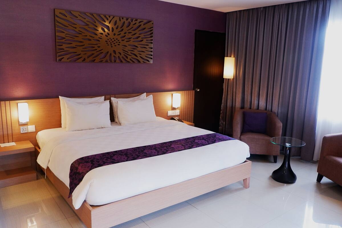 Hotelkamer met groot bed, twee nachtkastjes, een stoel, een tafeltje en een decoratief wandobject.