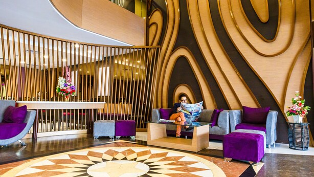 A modern lobby with a geometric patterned floor, a reception desk, purple seating, and a decorative wall with wood paneling. - Asialink Easy by Prasanthi (Batam)