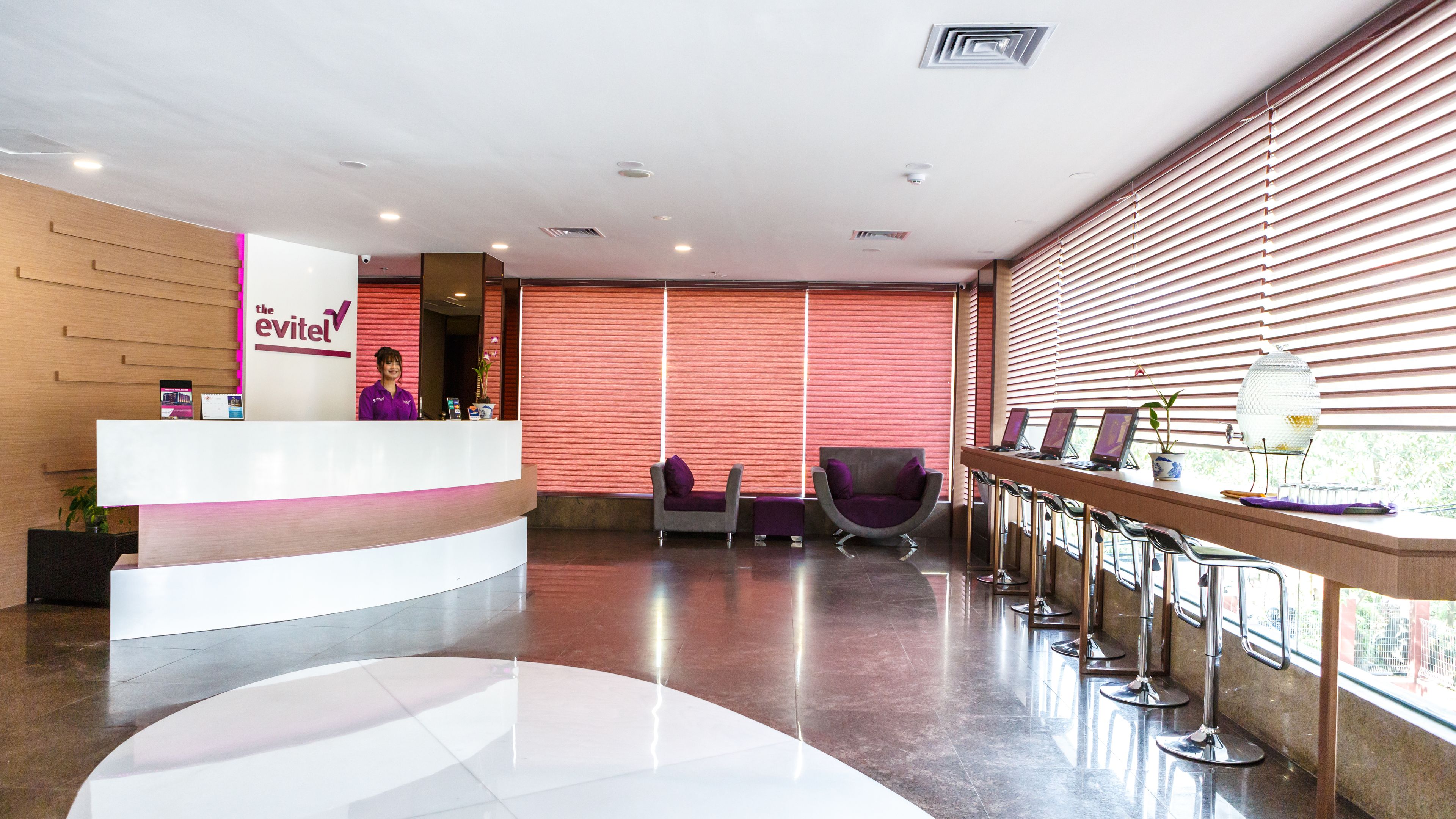 A hotel reception area with a modern design, featuring a reception desk, seating area, and a view of the outdoors through large windows.