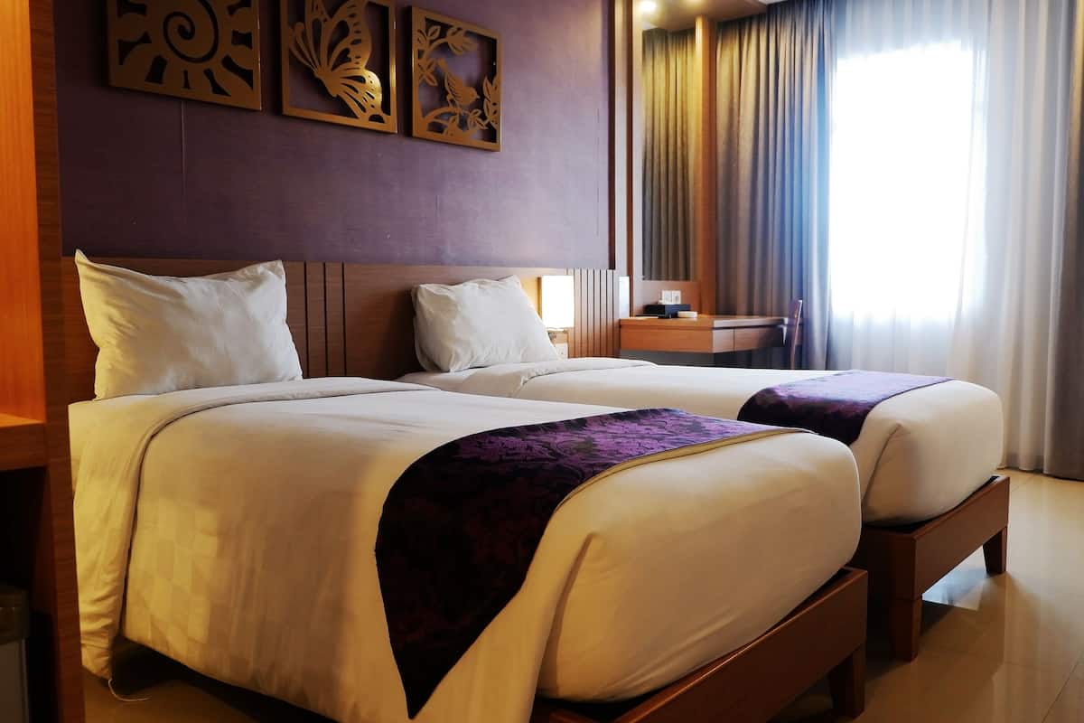 Een hotelkamer met twee bedden, een houten hoofdbord, een nachtkastje, een bureau en een raam met gordijnen.