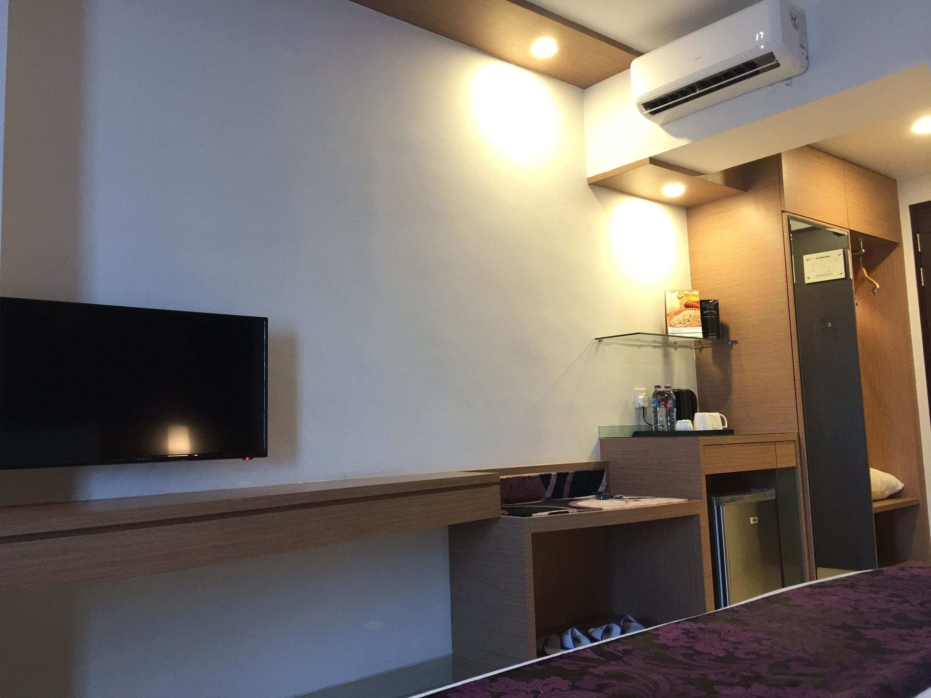 A modern hotel room with a flat-screen TV, built-in air conditioning, a glass shelf with toiletries, and a compact refrigerator.