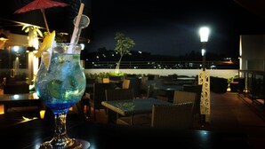 A cocktail on a table with a view of the night sky and distant city lights. - Asialink Easy by Prasanthi (Batam)