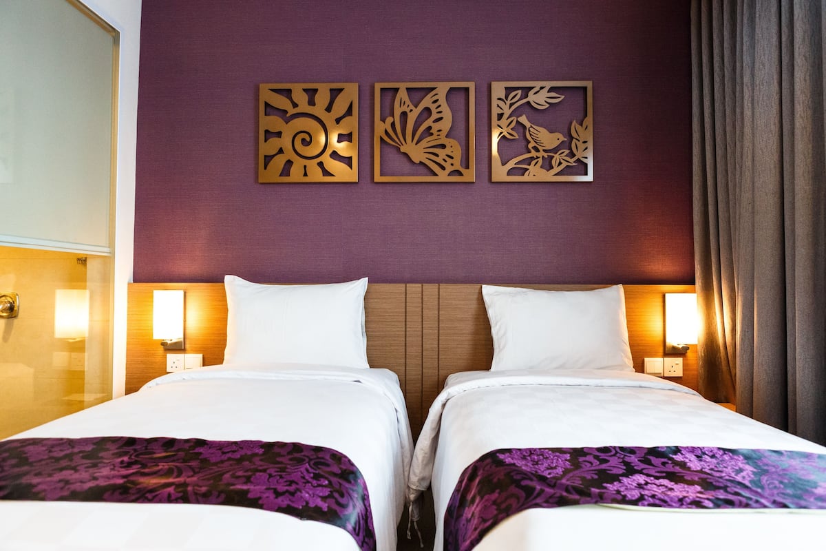 Een hotelkamer met twee bedden, een paarse muur en decoratieve wandkunst.