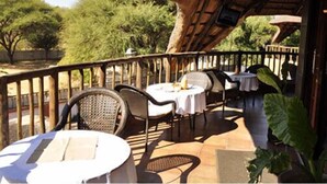 Un área de comedor al aire libre con mesas y sillas, rodeada por una cerca de madera y follaje.