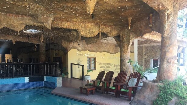 Un área de piscina interior con techo de roca natural, sillas de madera y una pequeña mesa.