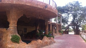 Un edificio rústico con fachada de piedra, una zona de estar cubierta y un camino pavimentado que conduce a una reja.
