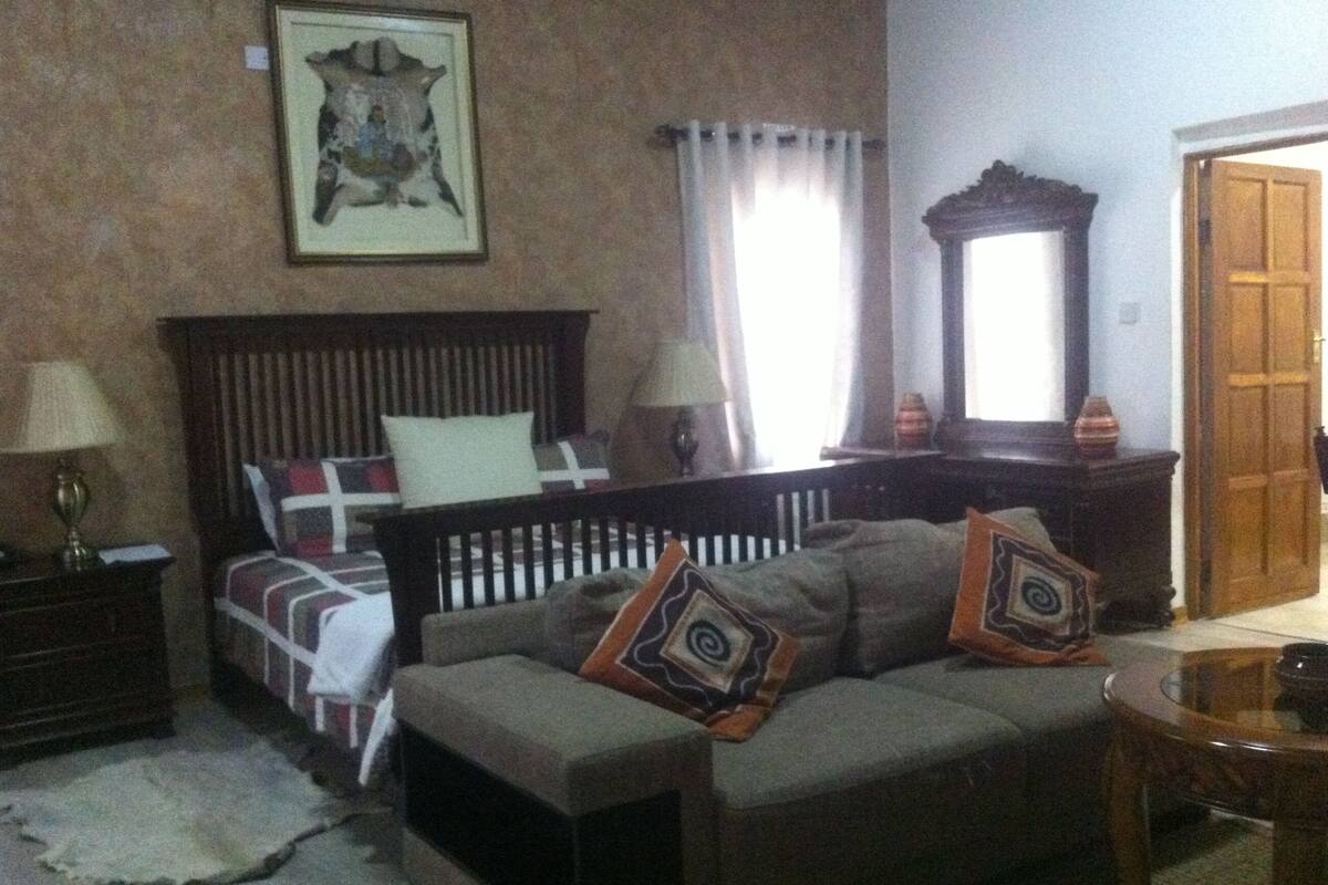 Ein Schlafzimmer mit einem Bett, einem Schlafsofa, einem Nachttisch, einer Lampe, einem Spiegel und einem gerahmten Bild an der Wand.