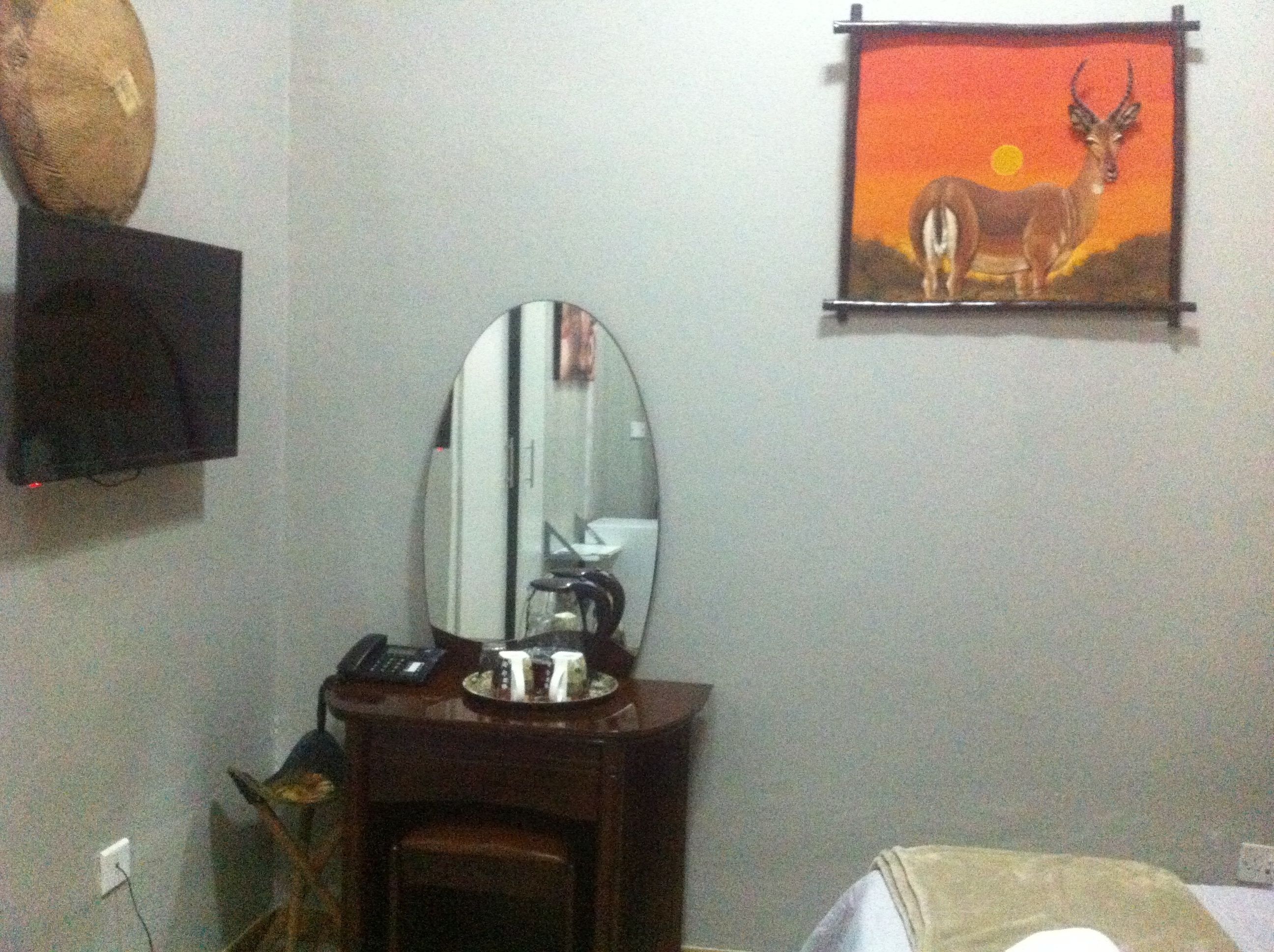 Una habitación con un escritorio de madera, un espejo, un teléfono y un cuadro en la pared.