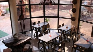 Un restaurante con mesas y sillas de madera, amplios ventanales y vistas a la calle.