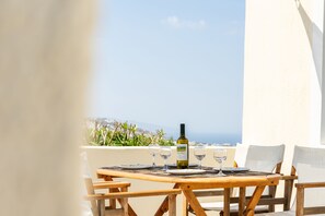 Mesa de madeira posta para refeição com garrafa de vinho, copos e pratos, com vista panorâmica.