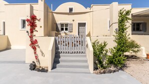 Ein Gebäude mit weißer Fassade, einem Tor und einem kleinen Garten mit roten Blumen und grünen Sträuchern.
