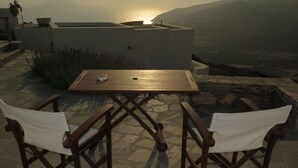 Eine Terrasse mit Tisch und zwei Stühlen, mit Blick auf eine malerische Landschaft aus Meer und Bergen.