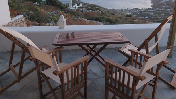 Eine Terrasse mit Tisch und Stühlen mit Blick auf eine Küstenlandschaft, eine Berg und das Meer.