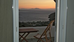 Ein Zimmer mit Meerblick bei Sonnenuntergang, ein Holztisch und ein Klappstuhl.