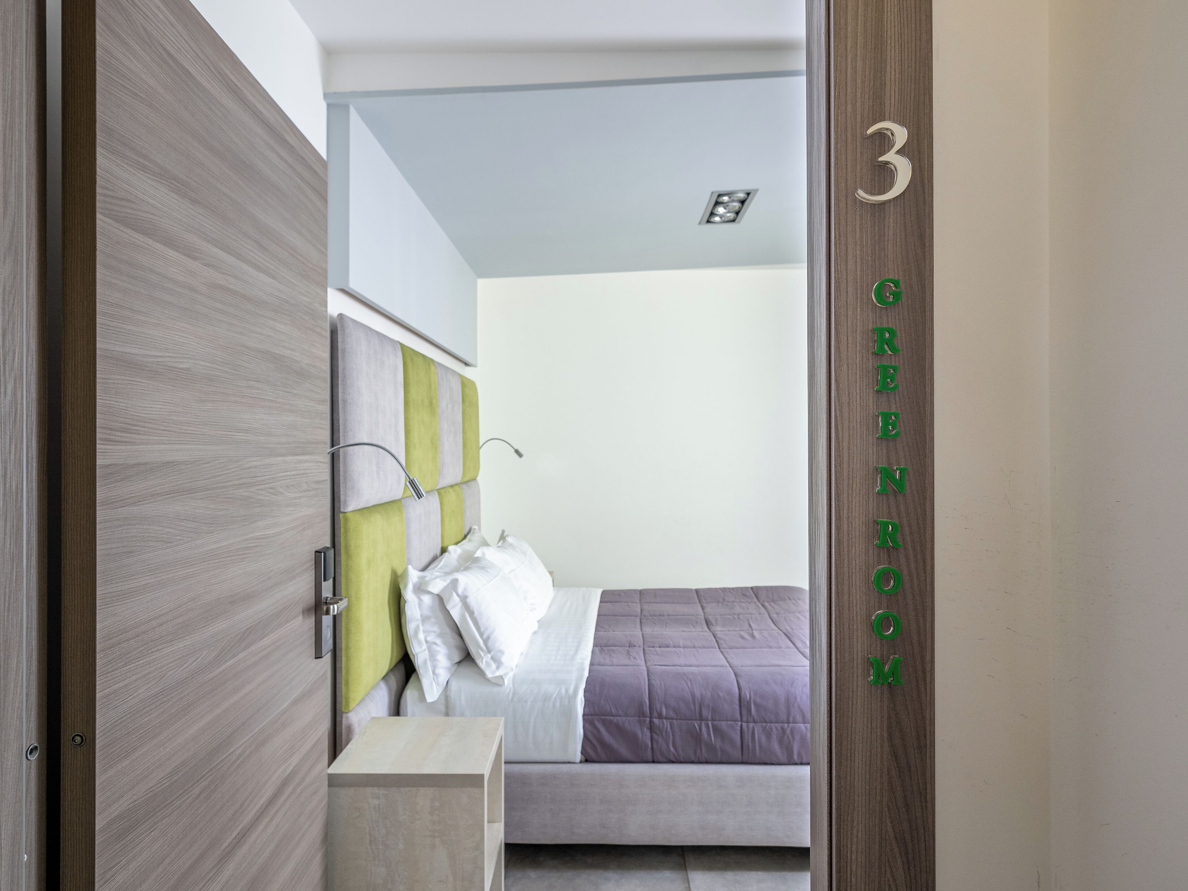 Un dormitorio con cama, mesita de noche y una puerta con número.