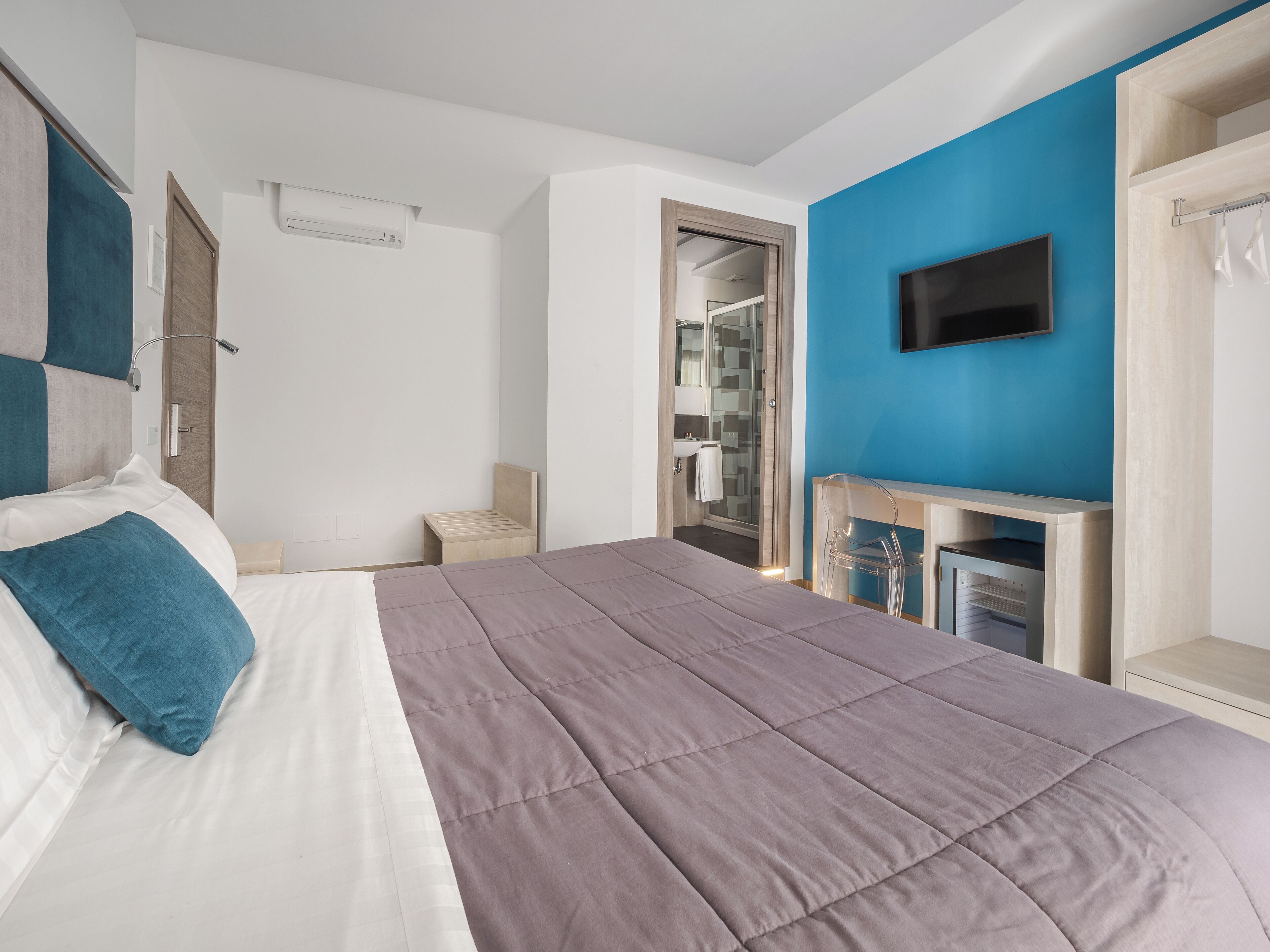 A modern bedroom with a bed, a TV, and a bathroom visible through an open door.