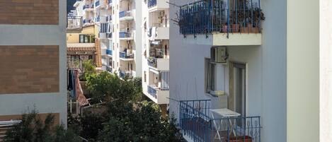 A row of multi-story residential buildings with balconies, some with plants, and a clear sky.