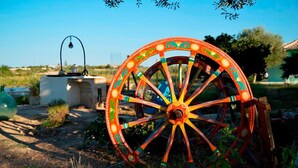 A large, colorful wooden wheel with intricate designs, set in a natural outdoor environment with greenery and a clear sky.