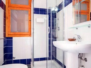 A bathroom with a white sink, a glass shower enclosure, and blue and white tiles.