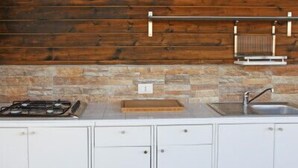 A kitchen with white cabinets, a stone backsplash, a gas stove, and a hanging rack above the sink.