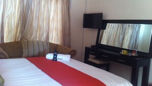 Hotelkamer met een bed, een rode deken, een fles Protex, een televisie en een spiegel.