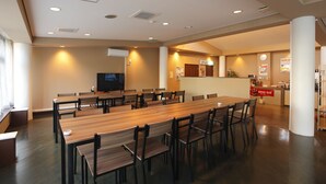 Une salle de conférence spacieuse, avec une longue table en bois et des chaises, un téléviseur et un bar à boissons à l’arrière-plan.