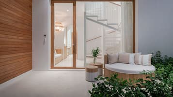 Un intérieur moderne avec un plancher en bois, un coin salon doté de coussins, un escalier et une porte en verre donnant sur une salle de bain.