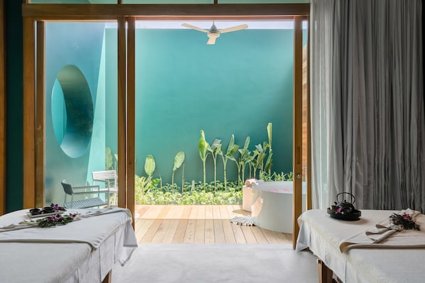 Un cuarto de spa con dos camas, un ventilador de techo y vista a un jardín a través de un ventanal.