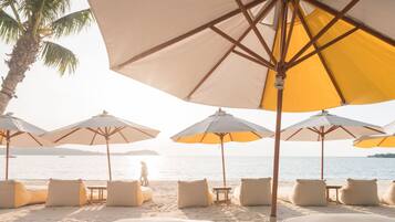 Un espacio de descanso en la playa con múltiples sombrillas y sillones, una mesa de madera y vista al mar.