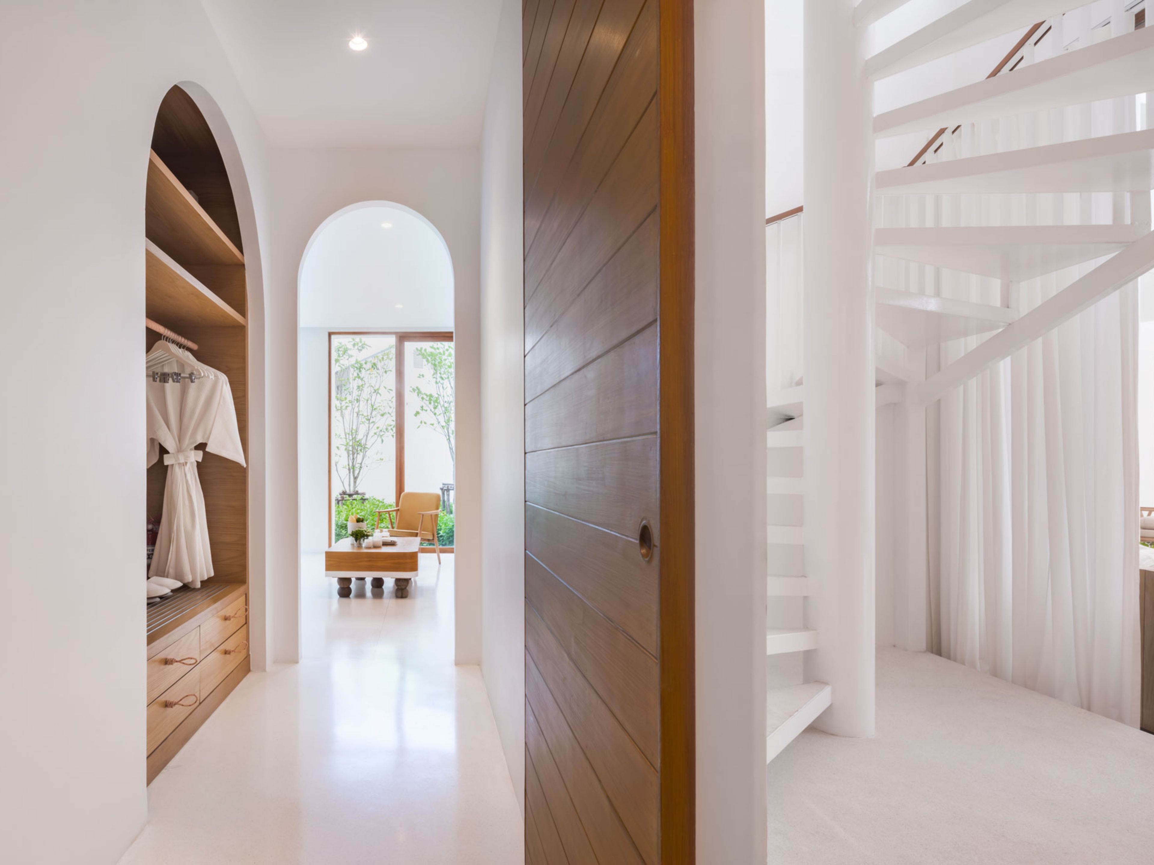 A modern interior with a wooden floor, white walls, and a staircase with white railings.