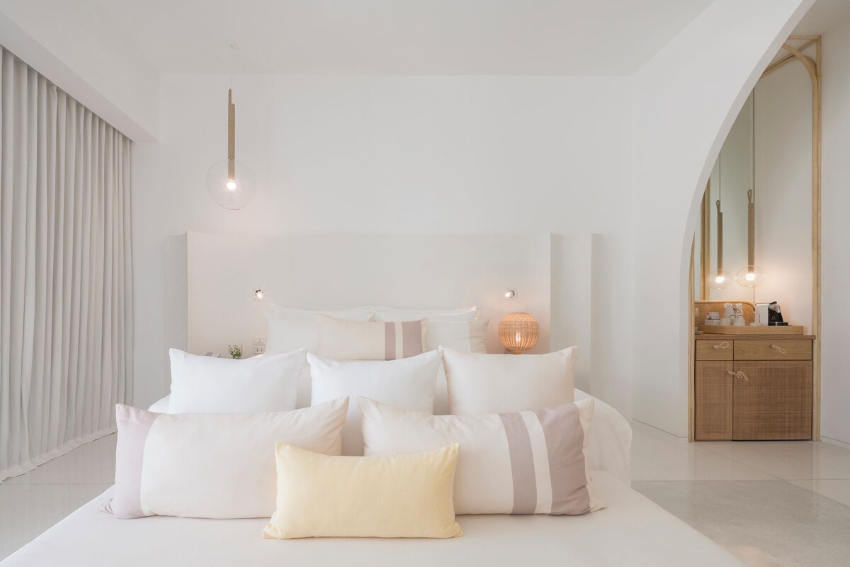 A modern bedroom with a large bed, bedside lamps, and a wooden dresser.