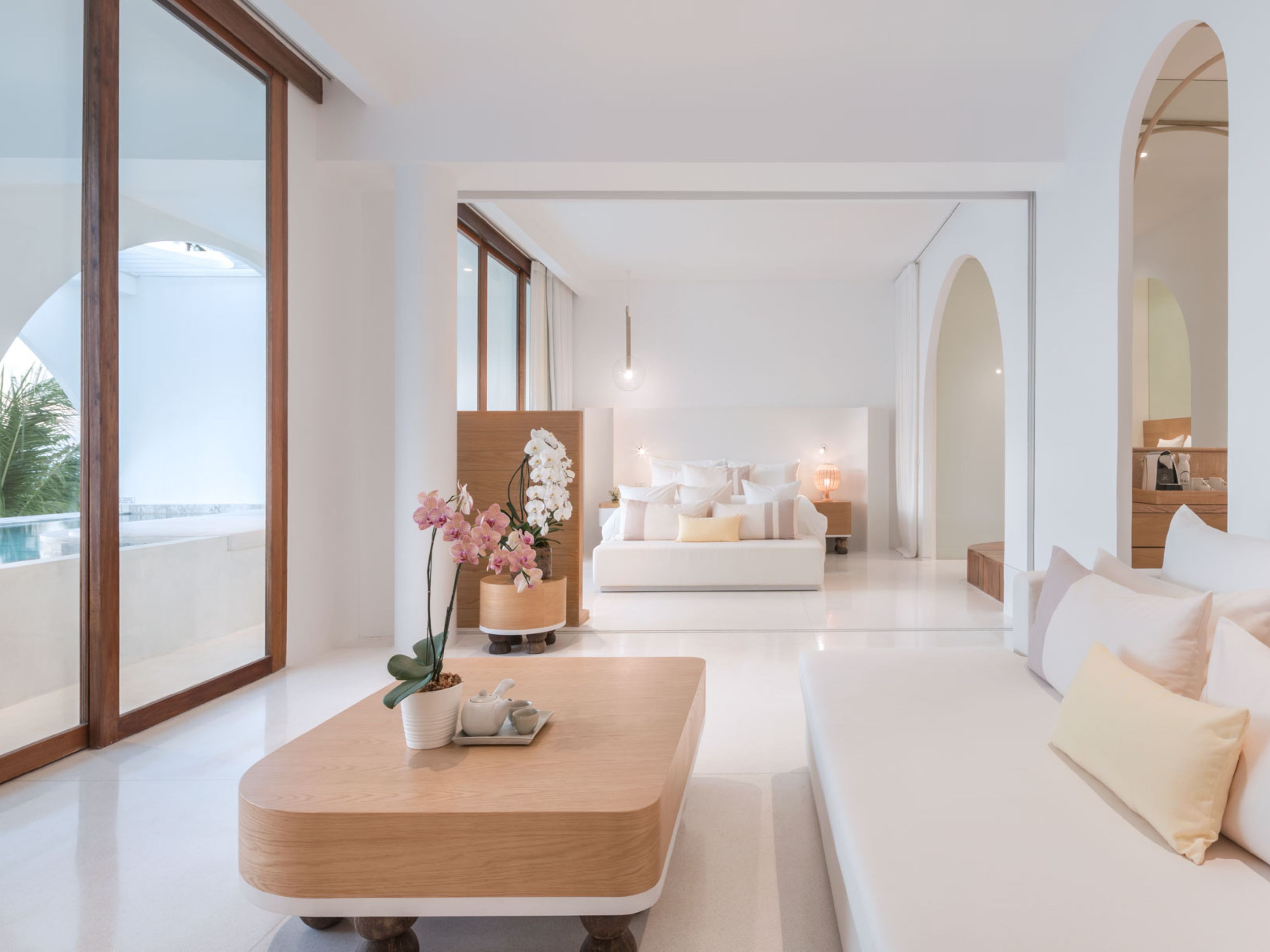 A modern living room with a wooden coffee table, a sofa, and a view of a pool through large windows.
