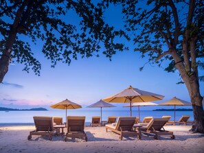 A beach with wooden lounge chairs and umbrellas, a clear sky, and a calm sea. - SALA Samui Chaweng Beach Resort (Koh Samui)