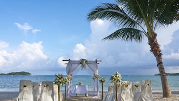 Een trouwceremonie op het strand, ingericht met een feesttent, bloemendecoraties en witte stoelen.