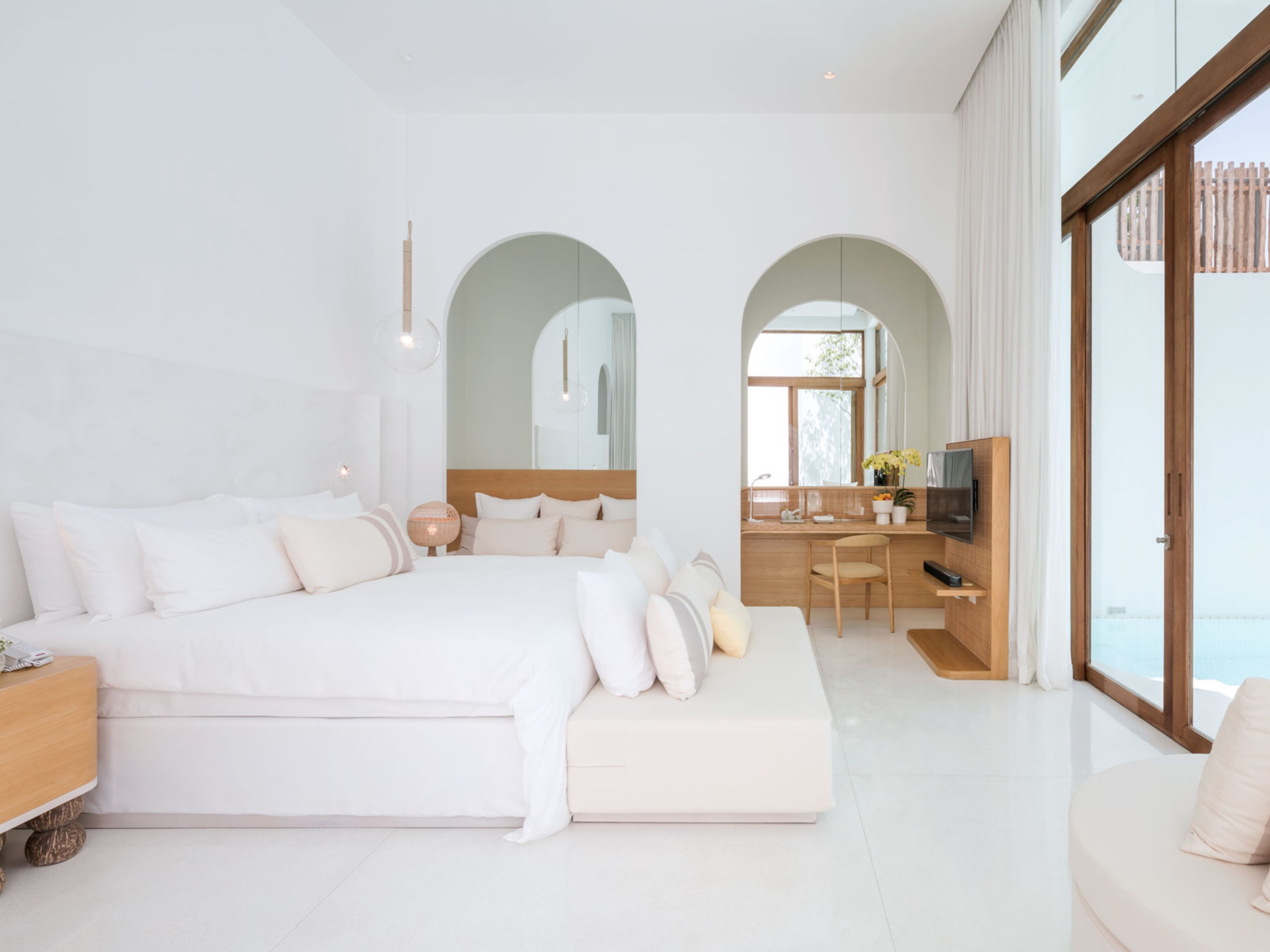 Une chambre moderne avec un grand lit, un bureau et une vue sur l’extérieur, accessible par une porte coulissante.